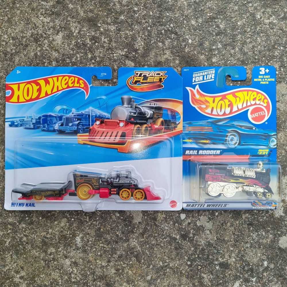 Beide Spielzeuge originalverpackt auf einer Betonfläche liegend. Nitro Rail sieht aus wie eine futuristisch gestaltete schwarze Dampflokomotive mit roten Akzenten, die allerdings goldgelbe Straßenräder hat. An Nitro Rail hängt ein kurzer einachsiger Anhänger in den gleichen Farben, auf den man ein weiteres Spielzeugauto transportieren könnte. Rail Rodder ist ebenfalls an eine Dampflokomotive angelehnt und überwiegend schwarz mit einem rot-gelben Flammendekor auf den Seiten. Seine hinteren Straßenräder sind aber hinter verchromten Abdeckungen versteckt, die wie Laufräder einer echten Lokomotive aussehen. Der Dampfkessel ist nur angedeutet, aus ihm heraus ragen zwei hintereinander liegende Motorblöcke. Rail Rodder hat keinen Anhänger.