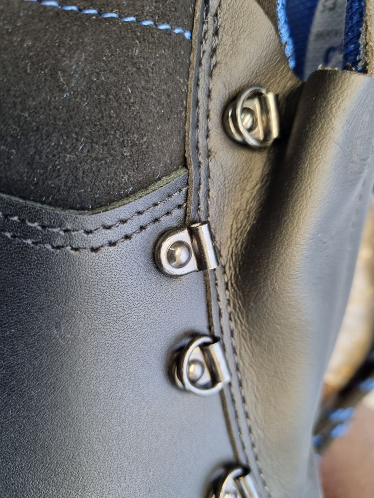 Eine Reihe an Leder festgenietete D-Ringe, von denen einer fehlt, als Teil der Schnürung eines Schuhs