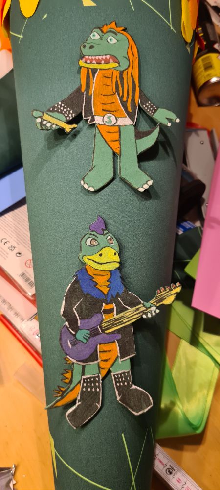 Die Moosgummi-Figuren von Mr Heavy Saurus und Muffi Puffi auf die vorbereitete petrol-neon-grün-farbene Schultüte mit Vulkan-Lava-Verschluss aufgelegt