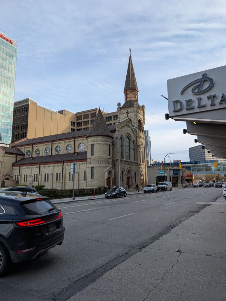 One of two old churches in downtown Winnipeg. Both over 150 yrs old.

Made of a light stone, it has a steeple that reaches for the sky and many round windows along the side.