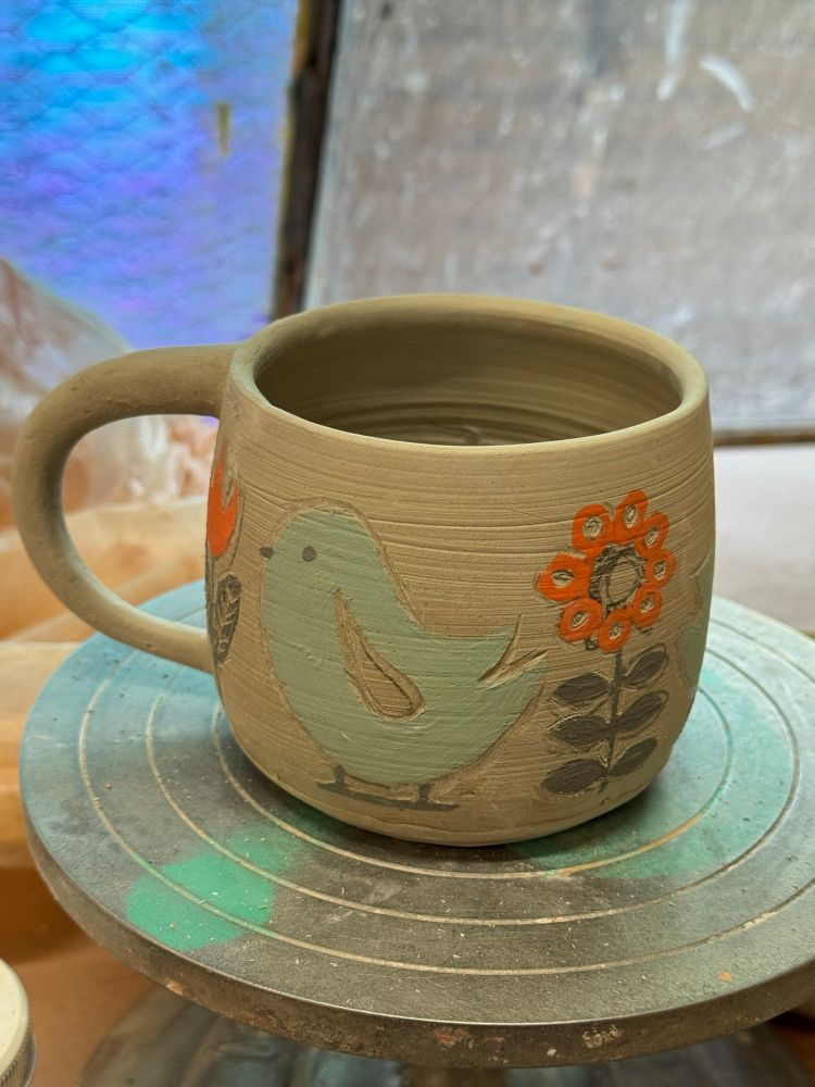 Coffee cup, greenware, painted with a stylized Scandinavian influenced design of teal birds and orange and black flowers 
