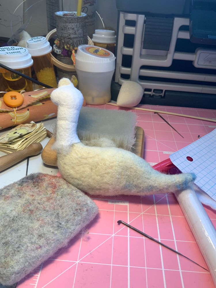 A work in progress needlefelt dinosaur on a messy work table.