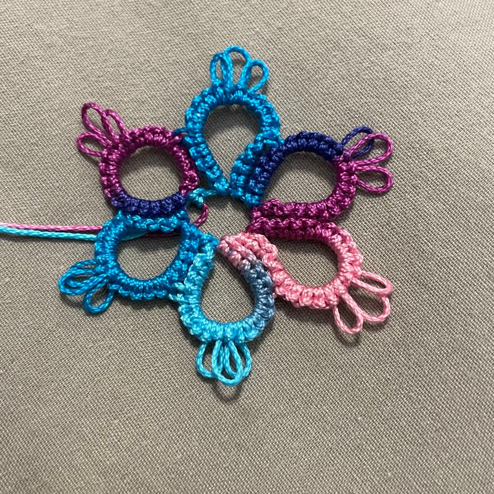 Small tatted lace flower in shades of purple, blue, and pink.
