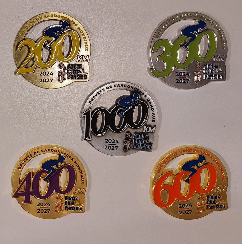 5 Medallien.
Inschrift in jeder Version: 

Brevet de Randonneurs Mondiaux.
2024-2027
Audax Club Parisien

Je eine Medaillie fuer 200, 300, 400, 600 oder 1000km Brevets.
