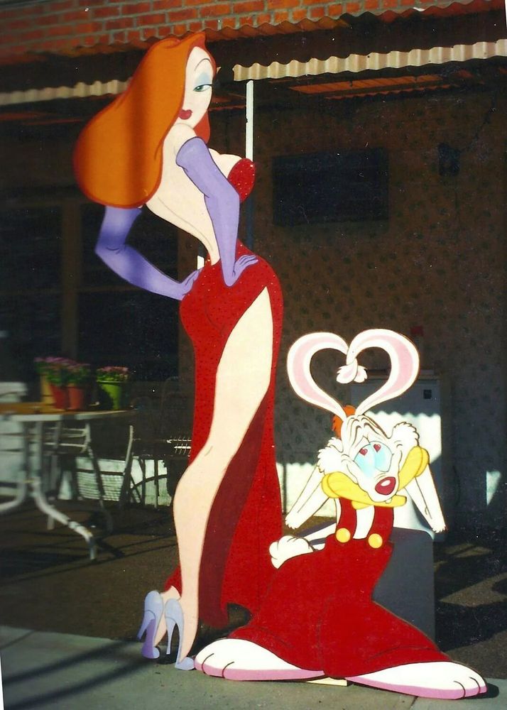 A photo of the characters Jessica and Roger Rabbit out on a sunny patio. Jessica Rabbit has both hands on her hips, looking aloofly over her shoulder. Roger Rabbit looks up lovingly at Jessica, hearts in his eyes and with his long rabbit ears forming the shape of a heart.