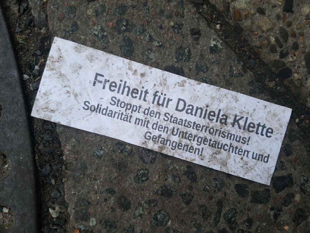 Weißer Zettel auf Steinboden mit der Aufschrift: 
Freiheit für Daniela Klette!
Stoppt den Staatsterrorismus!
Solidarität mit den Untergetauchten und Gefangenen!