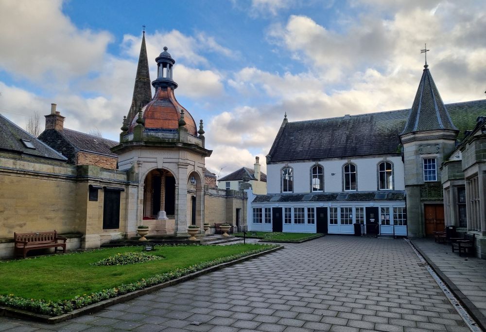 Shows the war memorial quadrangle just off the high street in the Scottish Border town of Peebles. The war memorial has bronze dome roof.
