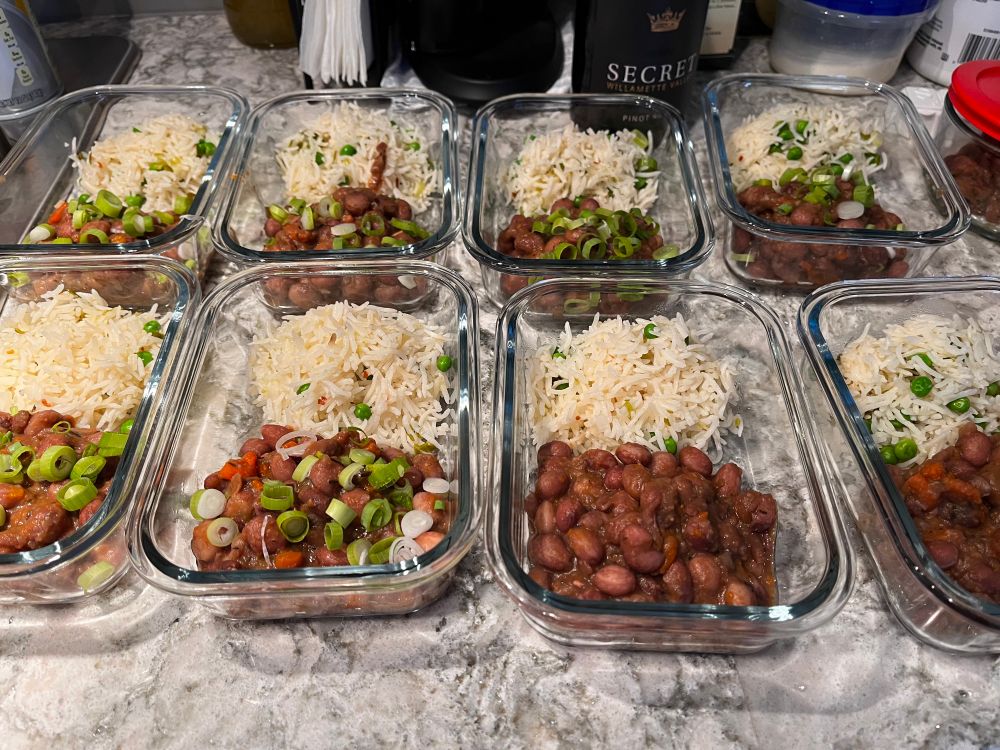 Eight rectangular glass dishes lined up in two rows of four on a white counter. Each dish holds a portion of rice and beans.