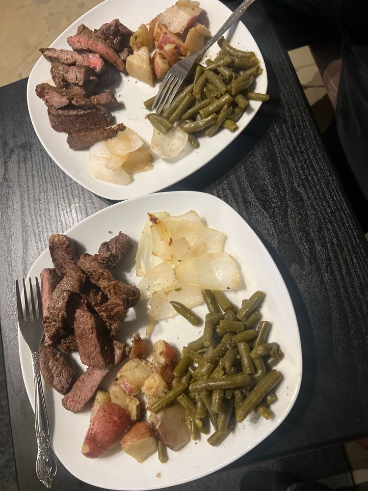 Two plates of steak, roasted potatoes, onions and green beans