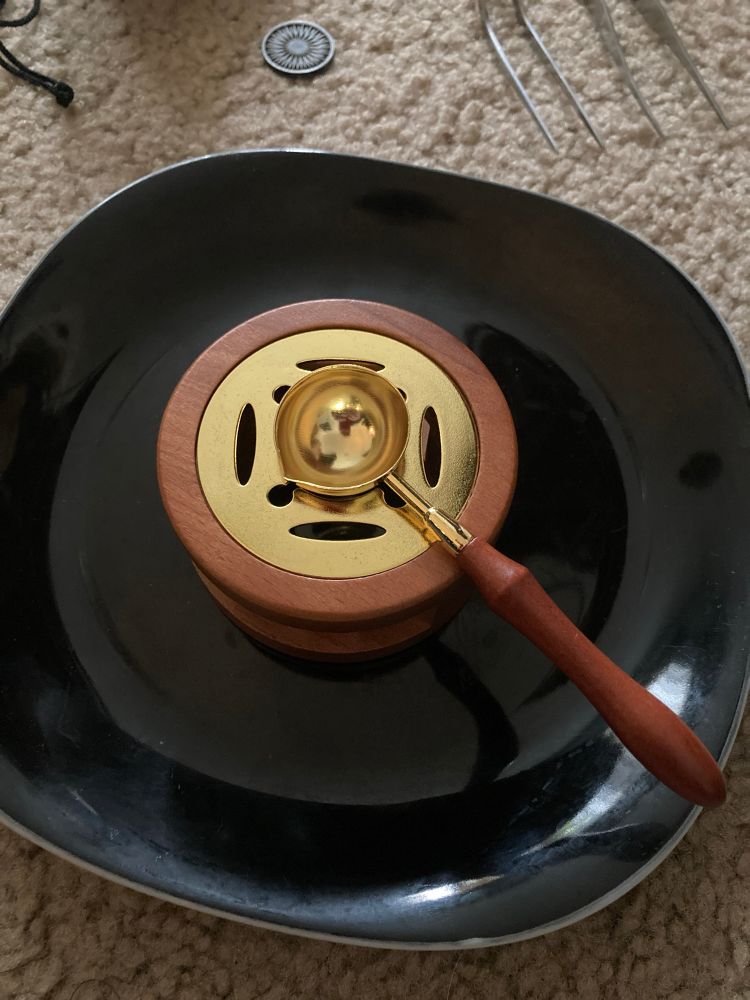 A small sealing wax melting set comprised of a copper spoon with pour spout and wooden handle set atop a matching wooden and copper holder for a tea candle.