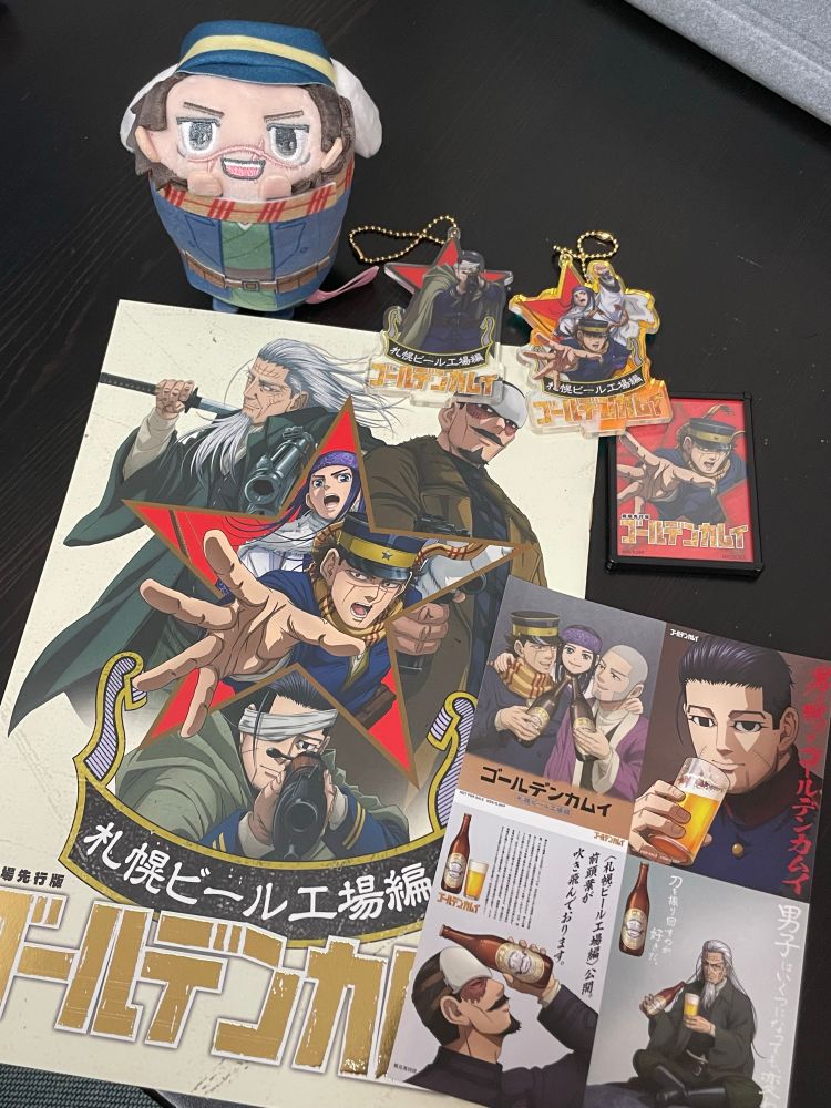 ゴールデンカムイ札幌ビール工場編の映画のパンフレット、特典のステッカー、尾形とアシㇼパ、杉元のアクリルスタンド、ミニチュアポスター、サンリオとコラボした杉元佐一の俵形のぬいの写真