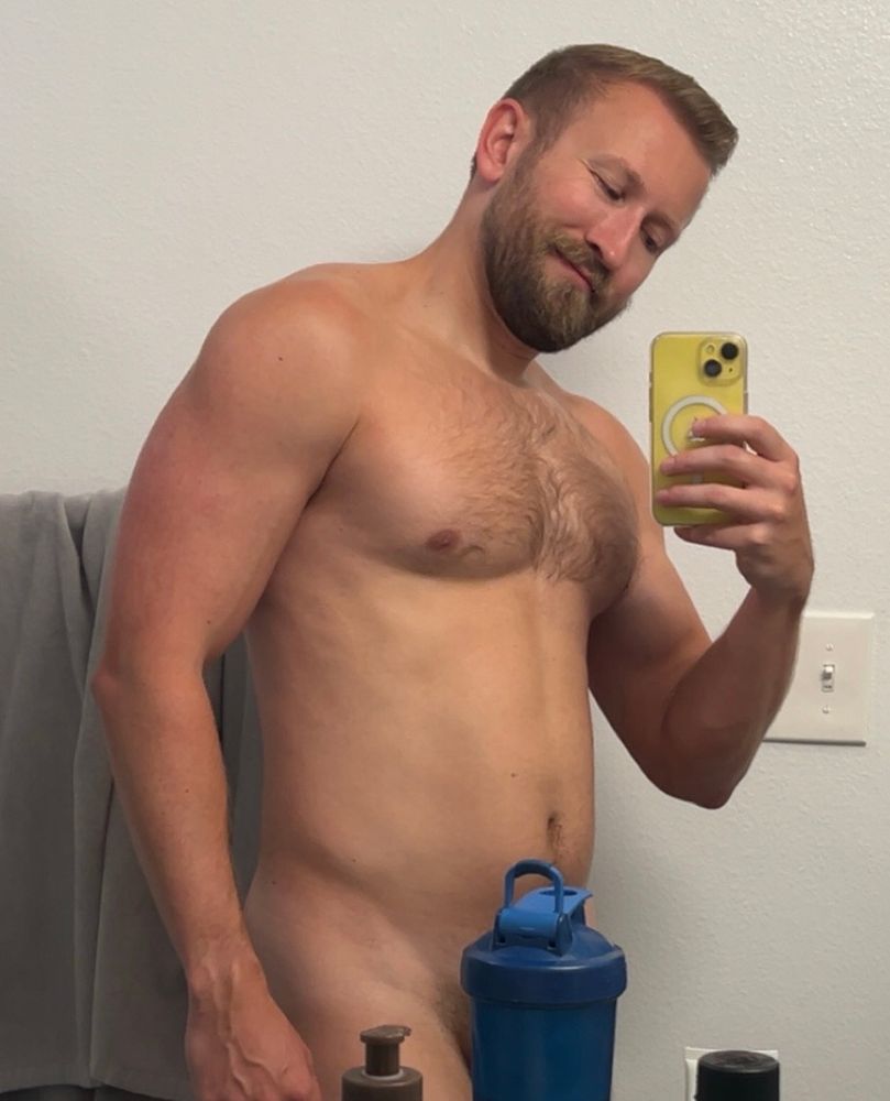 Mirror selfie of a naked man with a blender bottle covering his bits and bobbles