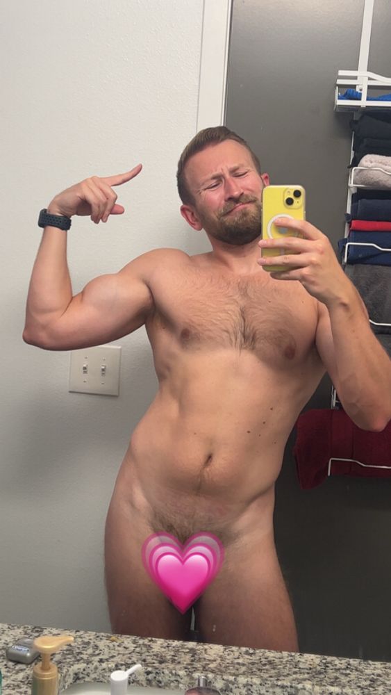Mirror selfie of a man flexing his bicep with a heart emoji over his crotch