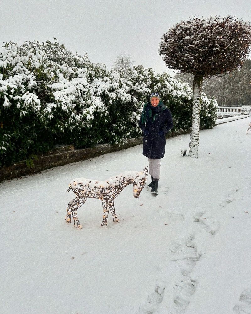 Micah standing in the snow next to a reindeer decoration and tree