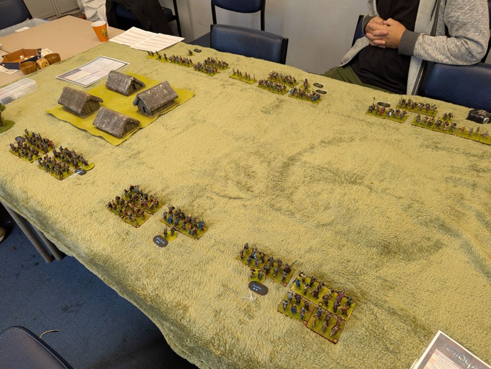 A wargames table with two armies and a village and hill