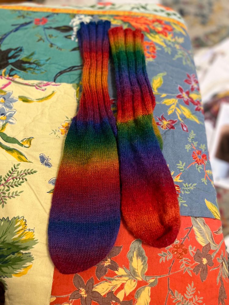 handknit 🧶 socks in a rainbow gradient. ancient crystal palace mini mochi yarn. one sock 🧦 much smaller than the other because kid wore to school for PE & it felted on her foot. 