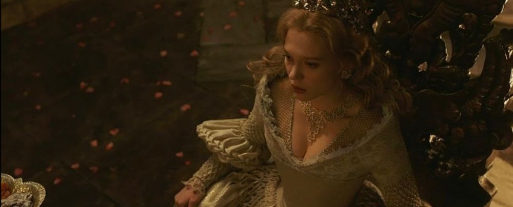 Lea Seydoux in La Belle et la Bete, wearing a white dress with intricate details and laces, her hair down, a crown and necklace.
