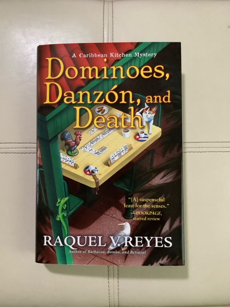 Book cover depicting Domino table with spilled coffee, cat, and ceramic rooster under shade typical of Miami’s Domino Park. 