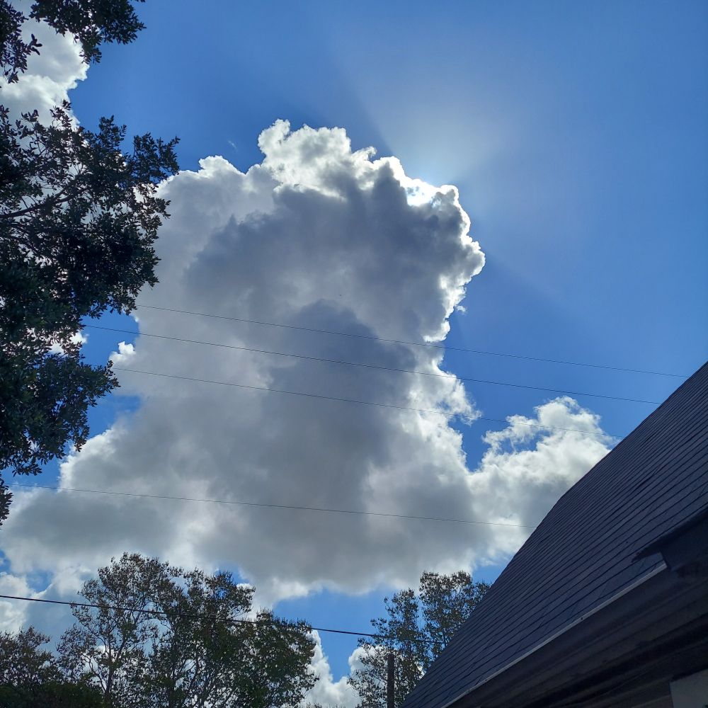 Against a pretty blue sky is a large white cloud with a hint of light beaming from behind it.
