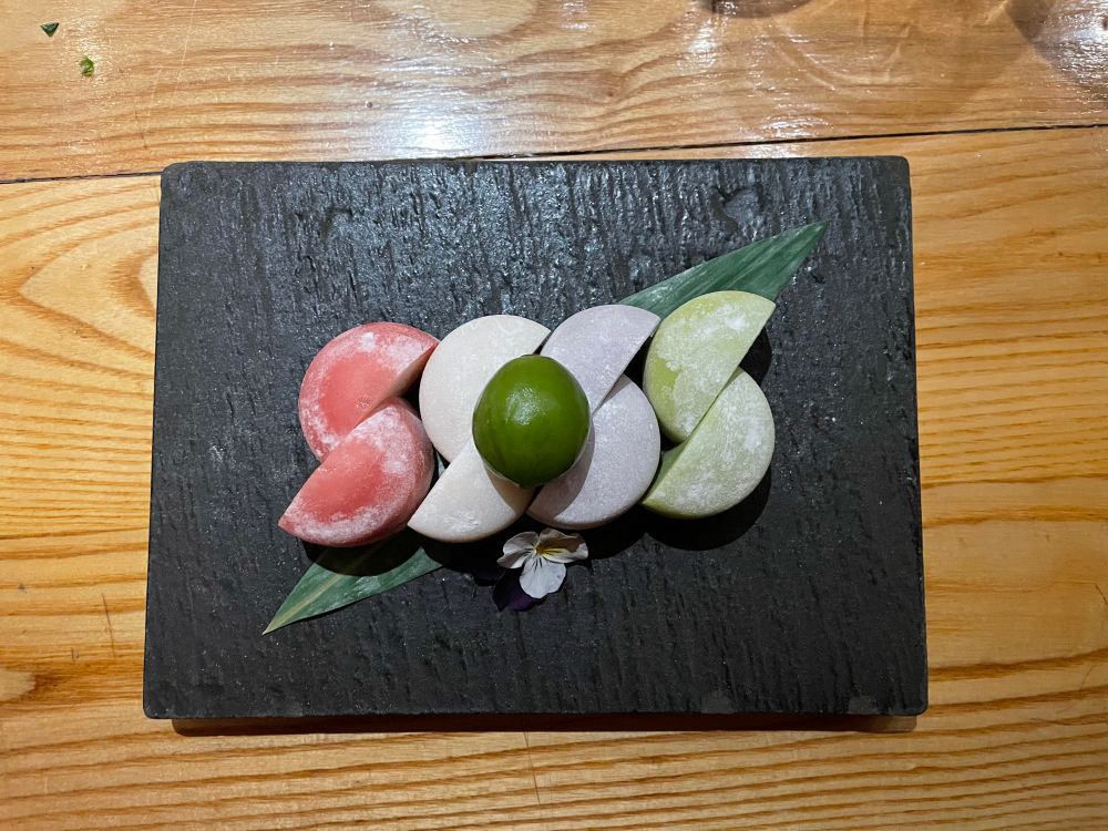 A slate board holding four pieces of mochi ice cream. 