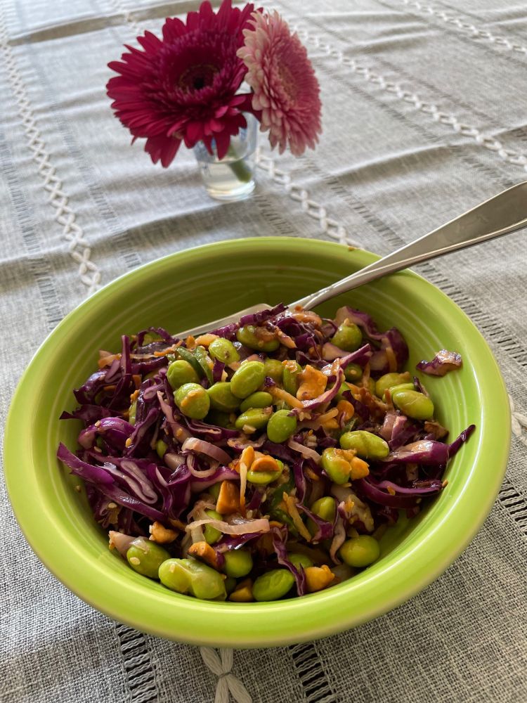 a green Fiestaware bowl filled with a salad of edamame and red cabbage, where the edamame match the color of the bowl. 