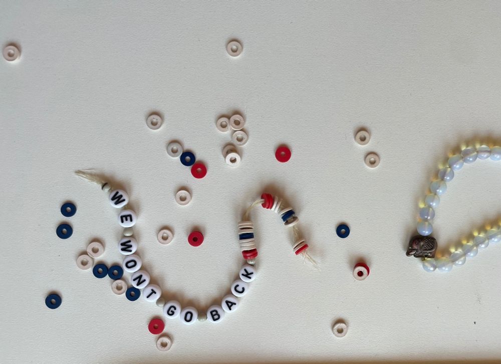 parts and loose beads of a bracelet spelling out WE WON'T GO BACK on a white desktop. 