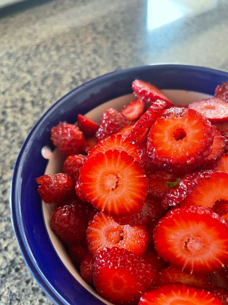 Closeup of strawberry slices in a ceramic bowl with a blue rim. 
