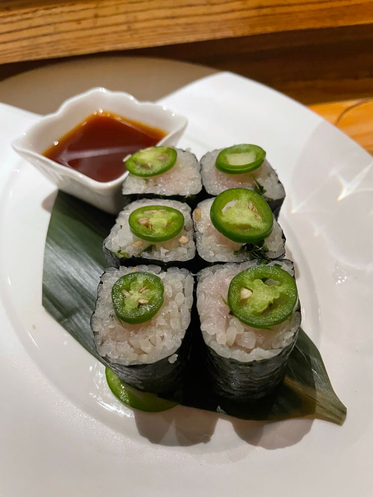 Closeup of several pieces of sushi, each with a bright green slice of jalapeño on it. 
