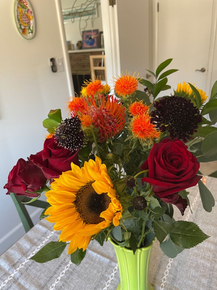 A bouquet of sunflowers, red roses, and orange spiky things whose name I don't know. 