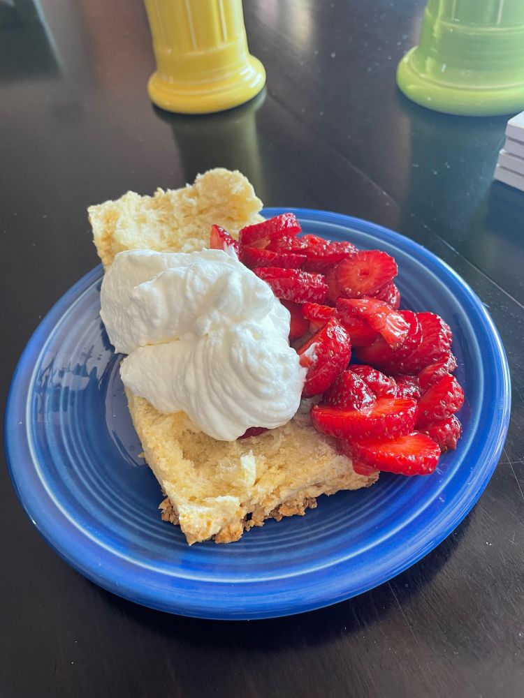 A strawberry shortcake with whipped cream on a blue fiesta ware plate on a black dining table. 