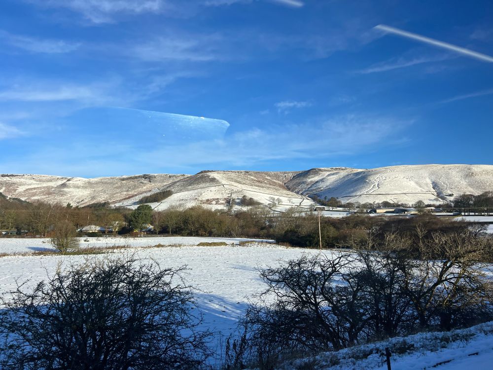 Photo taken from train window looking out at the Peak District hills covered in snow 
