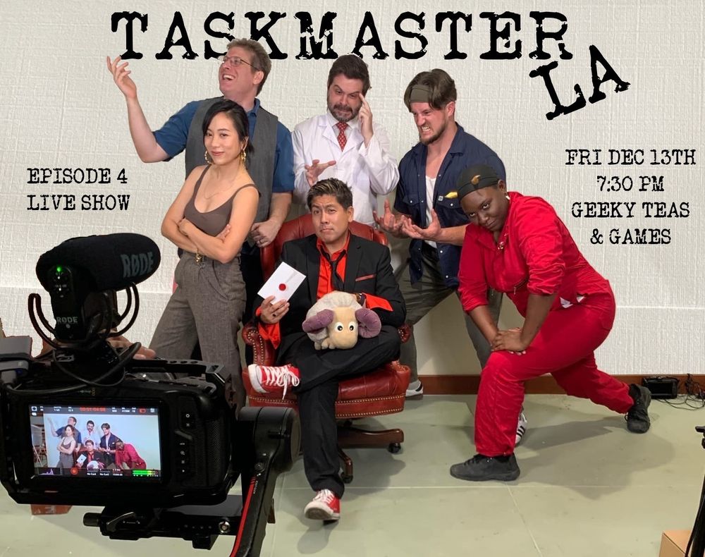 Contestants seated around the Taskmaster of Taskmaster LA around a red executive chair and holding a stuffed sheep. 
