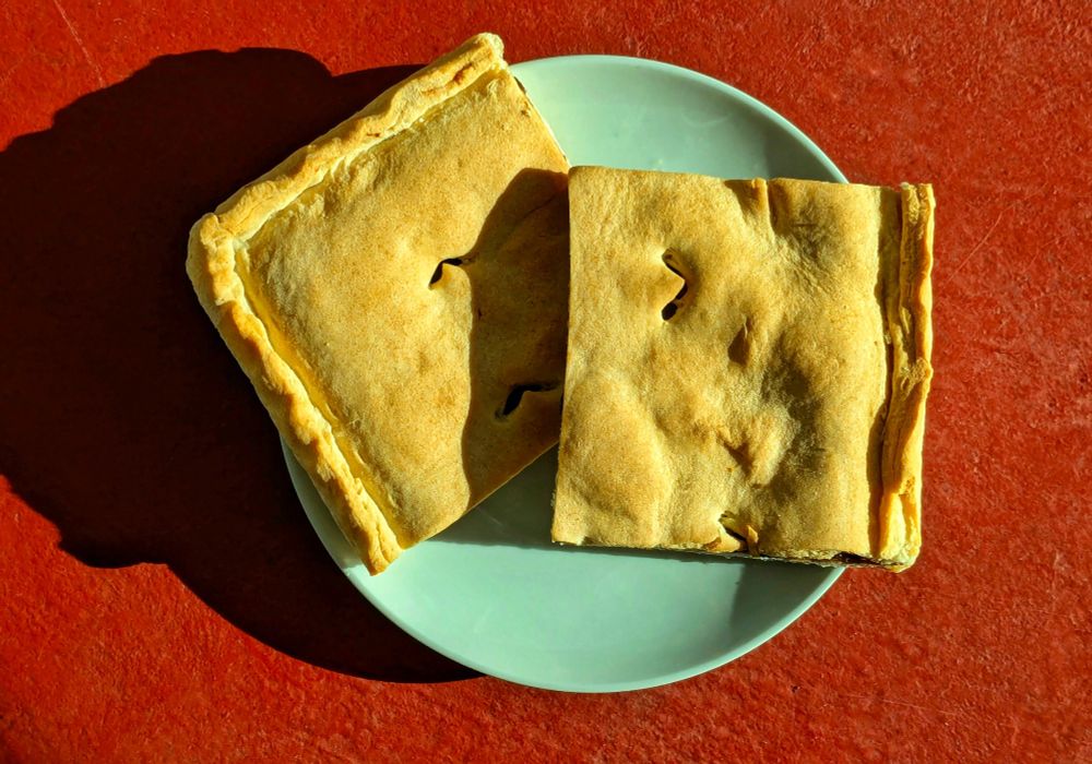 two square slices of prune sheet pie from the Pueblo of San Felipe rest overlapped on a light green desert plate against a sunny red background