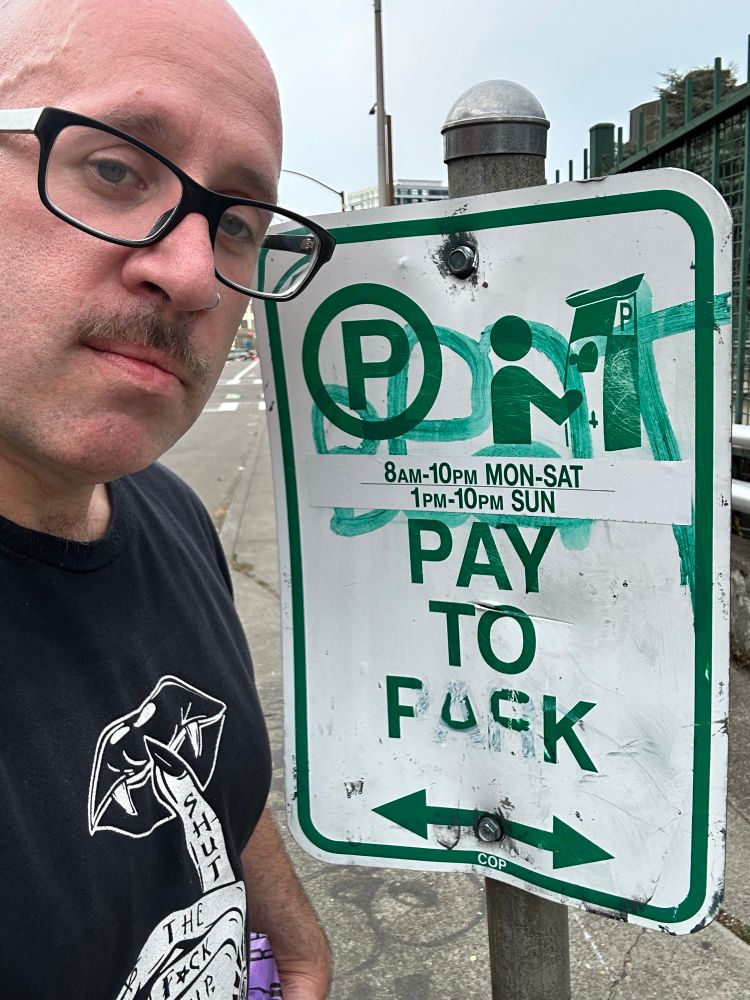 sangnoir stands next to a sign where someone has painted over the words pay to park to say pay to fuck