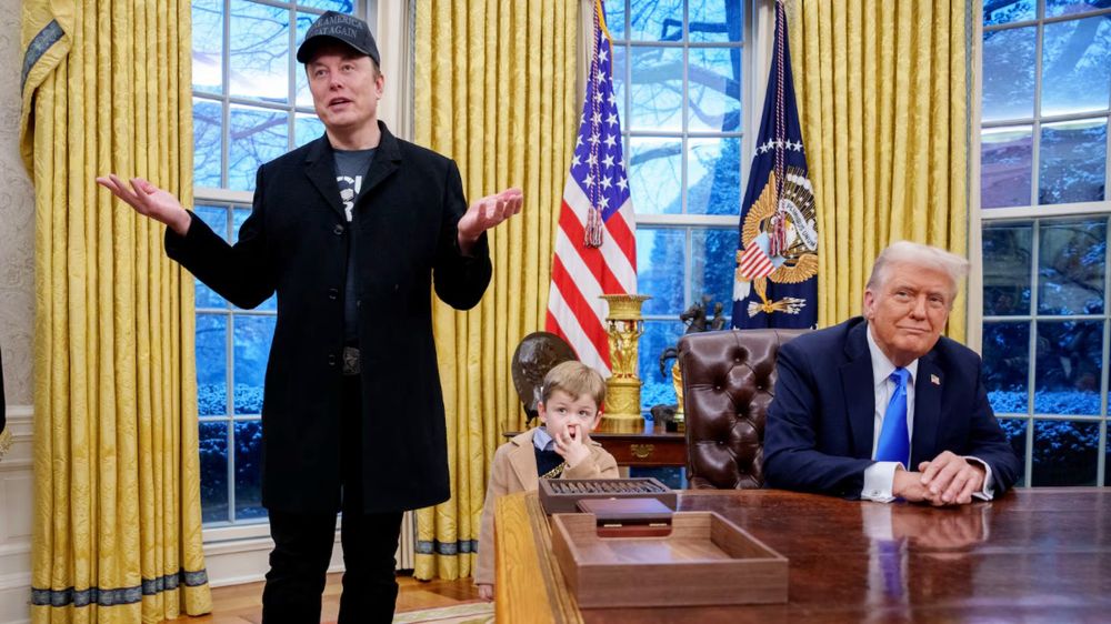 Photo of Trump sitting behind the Oval Office desk, with Elon Musk fielding questions from reporters while his 4-year-old son stands beside him.