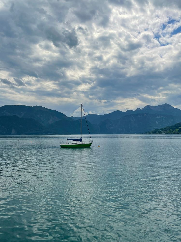 See mit Bergen im Hintergrund, auf dem Wasser ein Segelboot