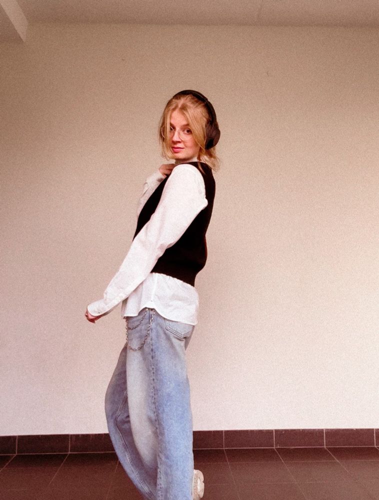 outfit picture , wearing a white shirt under a black sweater without arms, on top of blue jeans 