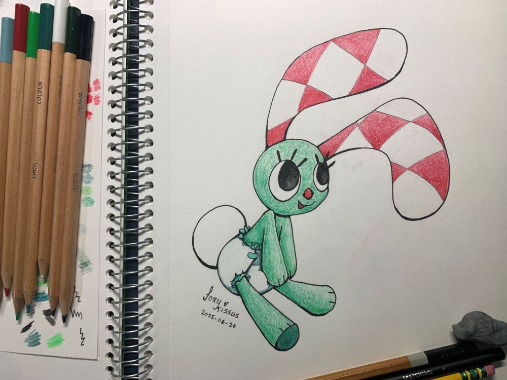 Fan art of the Rabbit with the checkered ears (A kockásfülű nyúl) created by Foxykissus in 2025. Traditional pencil art drawn in a spiral bound sketchbook. The lead character of a children's cartoon from Hungary, produced in 1977, created by  Veronika Marék.

The green rabbit poses with white and red checkered ears overhead, leans to the left, and wears a diaper. Pencils and an eraser frame the bottom and left of the image to show the tools and colors used for the picture.
