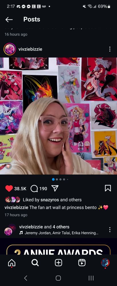 Vivziepop standing in front of a wall of fanart that's been displayed in the studio, my chaggie piece right there 