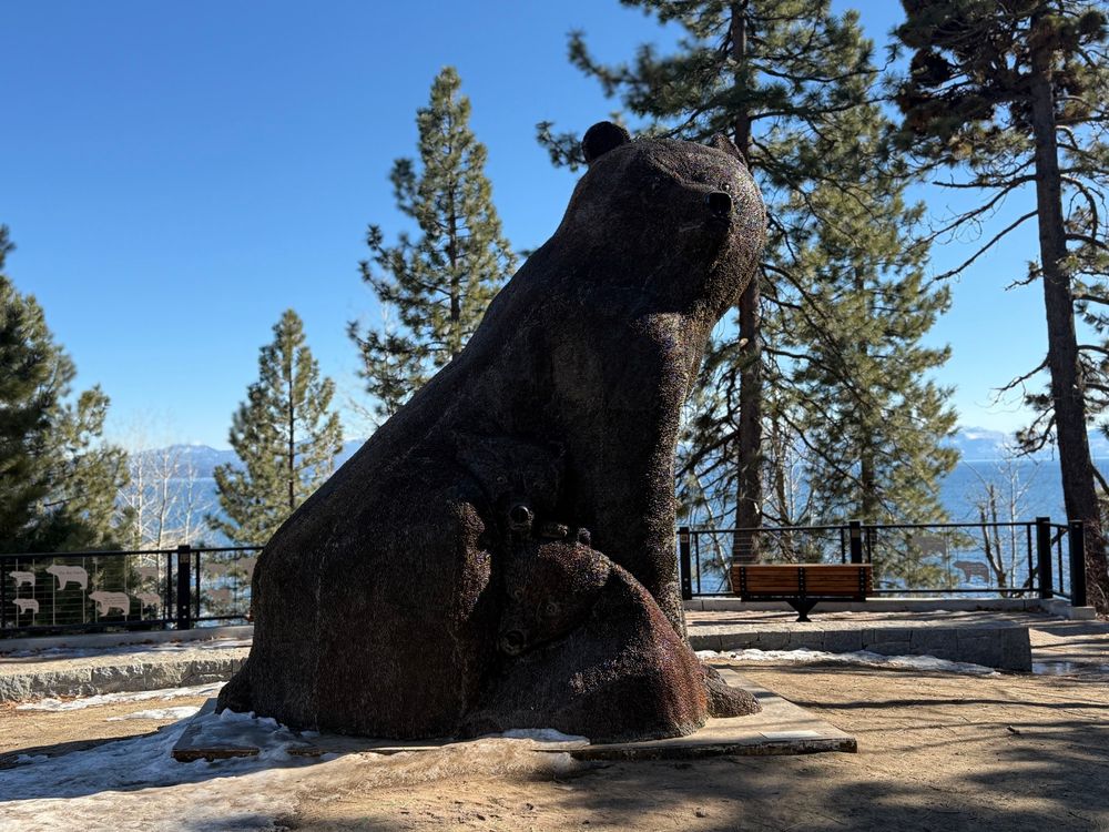 A large wooden statue of a mother bear and two cubs. Lake Tahoe is in the background 