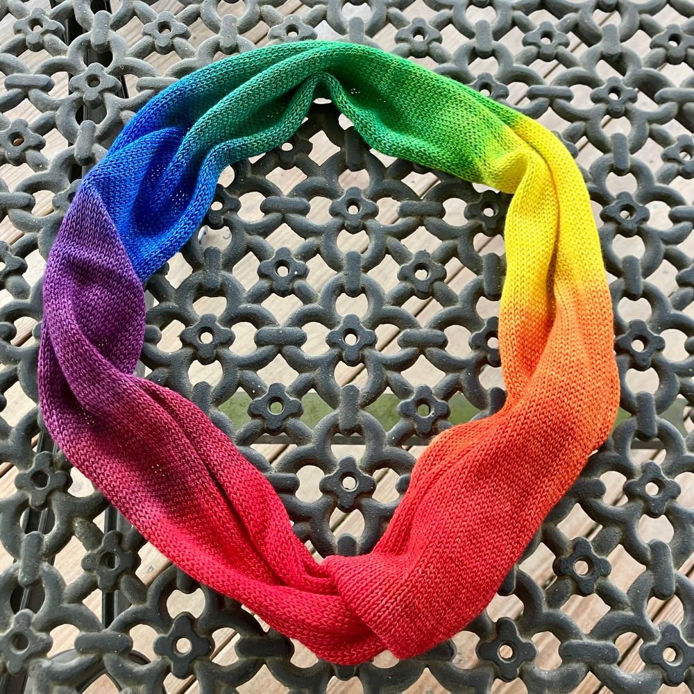 The knitted blank with the dye set, arranged in a ring to show that the beginning and ending reds match. The colors fade through the rainbow counterclockwise, with red at the bottom of the photo. The fabric is on a black deck table, the one that I would have preferred to dye the yarn on.