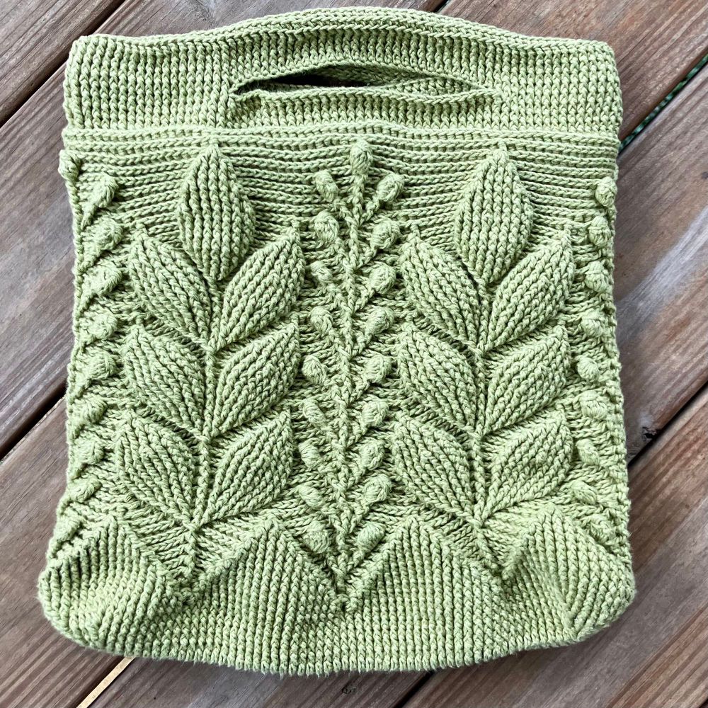 The complete but unlined crocheted body of a pale green Spica Embossed Bag, designed by Natalia Kononova, a.k.a. Outstanding Crochet. Embossed crochet uses a combination of front post and back post stitches to create a sort of bas relief texture that people (including the owner of my local yarn shop!) often believe is knitted at first glance. The rectangular bag has alternating branches of broad smooth leaves and branches of small flower buds running up the sides and slit handles at the top. There’s also a long strap, not pictured here, that I will attach once I’ve properly reinforced the handles and lined the body.  I’m 95% sure I used Rowan Creative Linen, a linen/cotton blend.