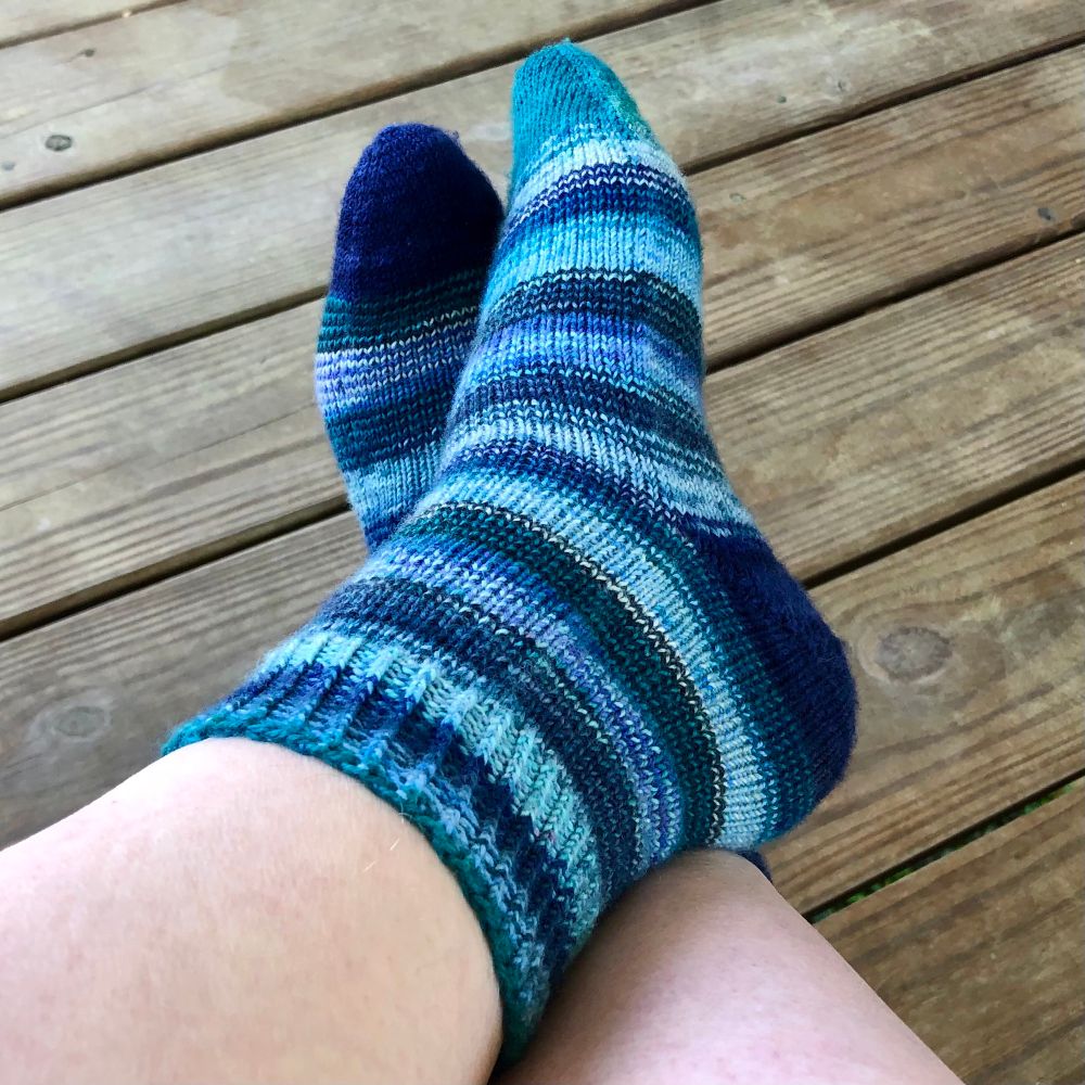 My feet in the blue-green-blue chaos socks, but crossed to better show the inside edge and heel of the left sock. I do a fair bit of show-off knitting, but my goal with these socks was to take a break from complicated patterns and enjoy the exquisite colors.  Vanilla Extract, the pattern I used for all three pairs of socks, is now my go-to nothing-fancy sock pattern. I experimented with several different types of ribbing for the cuffs; this pair has 1x1 twisted rib, which I particularly like for the muddled striping.