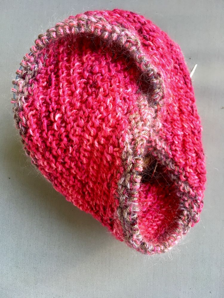 The in-progress cowl, shortly after I started the border. Since the cable needle runs through the entire edge of the möbius strip, the fabric is wrapped into a compact cowl. For fun, when I started the border, I made the diagonal texture slant in the other direction. So in the finished cowl, if you follow a stockinette or reverse stockinette stripe, it makes a W shape instead of a V.