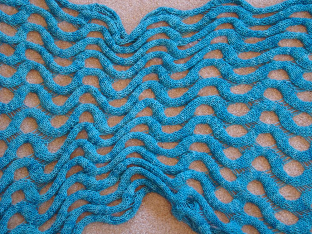 The middle of the unblocked Summit shawl. I spread out the rectangular shawl loosely and let the middle stay bunched up to show the drape and the depth produced by the curl of the unblocked strips of stockinette that undulate between the lines of drop-stitch framed holes. I will link this pattern (as well as the cardigan pattern) in a reply post. I knit this in the raw silk yarn from the pattern, in the same pale blue color.