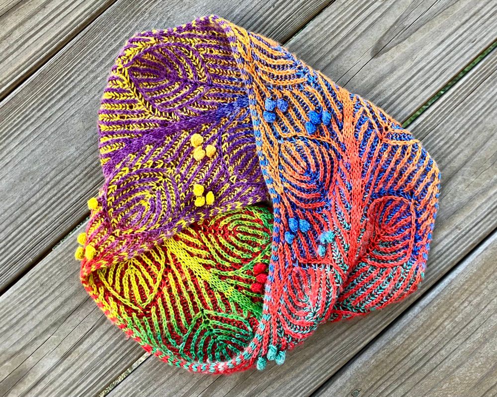 My second Double Rainbow Cover cowl, a Möbius cowl with only one surface and one edge. Here, it’s configured like the triangular three-arrow recycling symbol, but sideways. To the right is an uninterrupted strip of red/orange on purple/blue. The two segments on the other sides of the triangle are purple on yellow and yellow/green on red. My color transitions were smoother and more even than in the first cowl, but yellow to green was still patchier than I’d like. I did lose some vibrancy compared to the first cowl, so this one is has a more mellow color scheme.