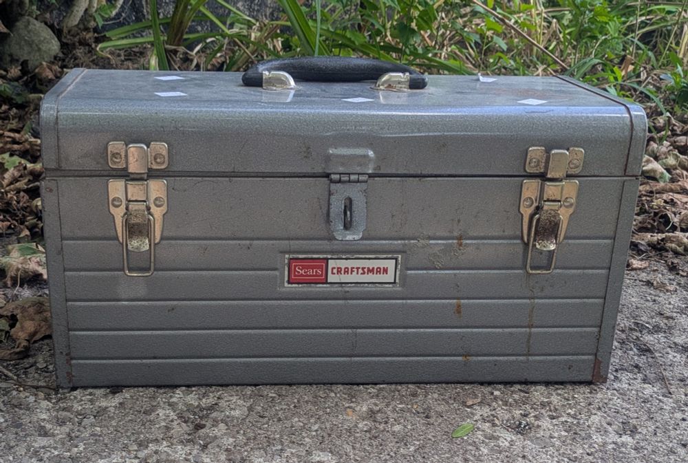 Front facing image of a grey vintage Sears Craftsman 1970s or earlier metal tool box. It has a gasp for a lock and two latches. 