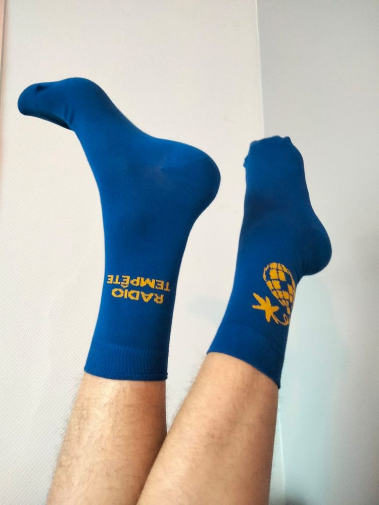 Photo de pieds en l'air avec des chaussettes bleues électriques avec écrit Radio Tempête en jaune.