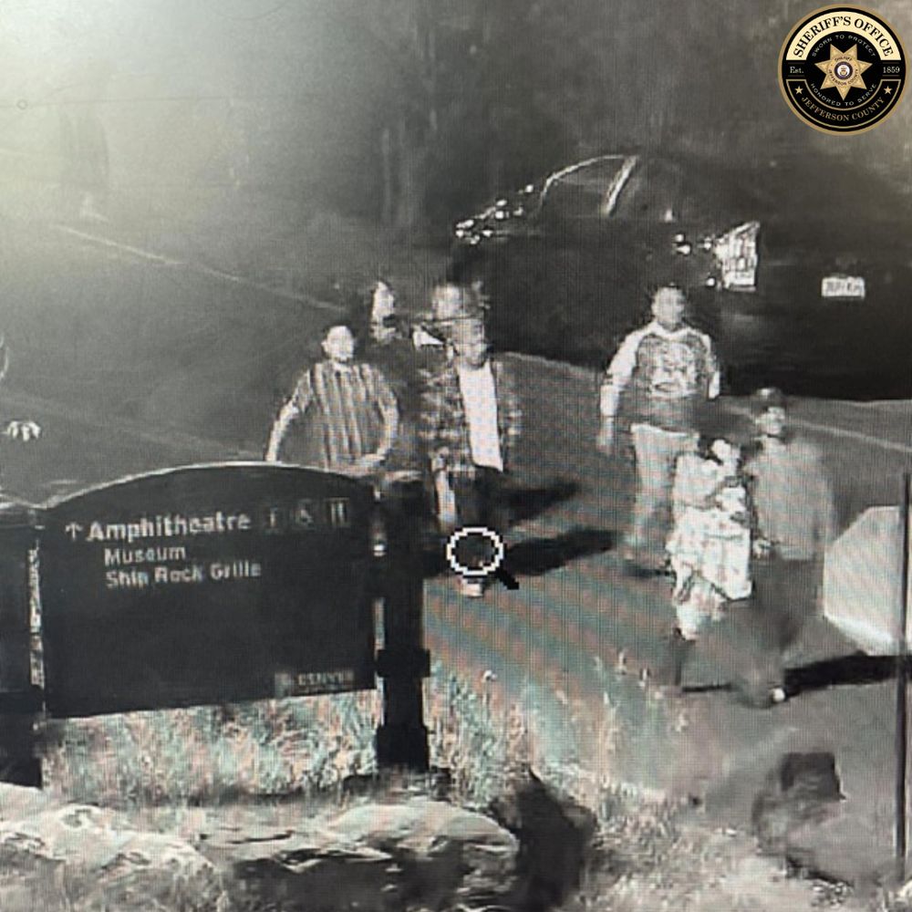 Night security camera view of five people walking past a Red Rocks sign on a paved path. Sheriff’s Office logo in upper right.