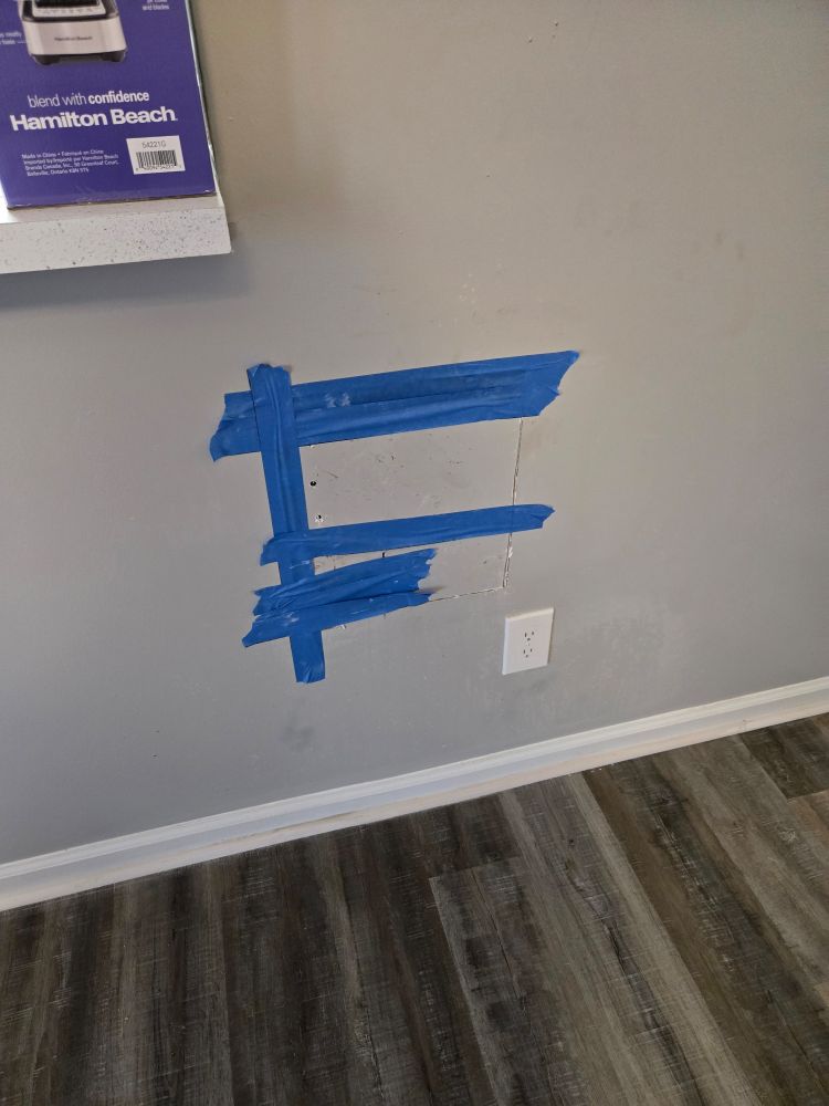 Hole in wall patched up temporarily with blue tape

